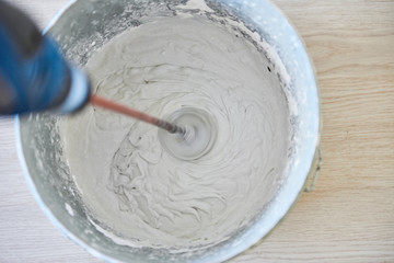 Worker mixing plaster in bucket using an electric drill.