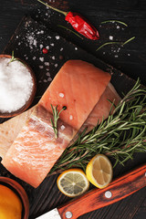 Salmon fish with rosemary on black wooden board.