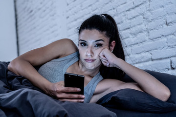 bored and tired pretty young woman using mobile phone in bed.