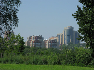 Obraz premium Urban high-rise buildings against a background of green trees and shrubs