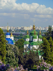Fototapeta na wymiar The tops of churches with golden domes on the background of the bridge across the Dnieper and residential buildings