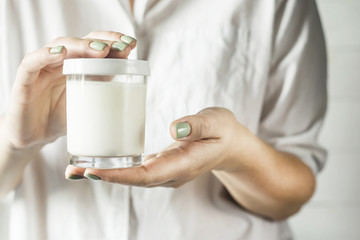 A glass jar with a white lid with homemade yogurt in the hands of a woman in a white shirt. Healthy diet breakfast