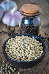 Dried white and black pepper corns with glass bottle on wooden background.