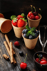 Summer berries for ice cream  in waffle cones on black wooden background.