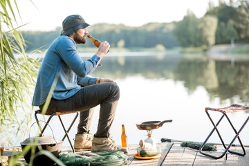 Handsome man relaxing with beer sitting alone during the fishing process on the pier near the lake