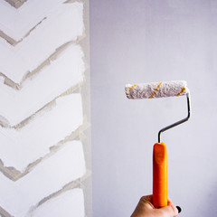 Painting a wall with masking tape. white zigzag strips on grey wall. hand holding the roller with...