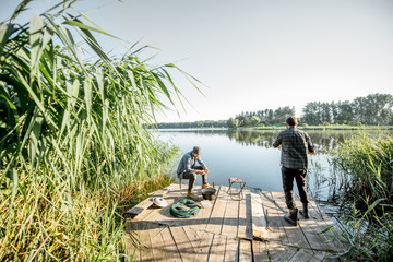 Two fishermen relaxing during the picnic on the beautiful wooden pier with green reed on the lake...