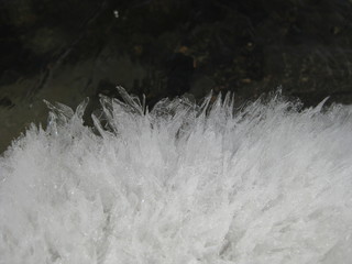 Ice crystals that appear when ice melts as a result of temperature changes. Crystals are like soft white wool. Ice crystals appeared near the water.  The snow melts and the water flows out of the ice.