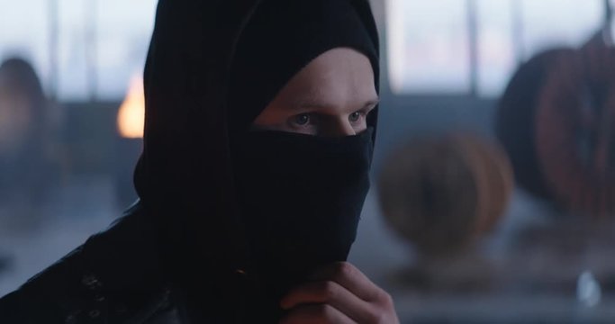 Riot man puts black balaclava in industrial background (4k, slow motion)