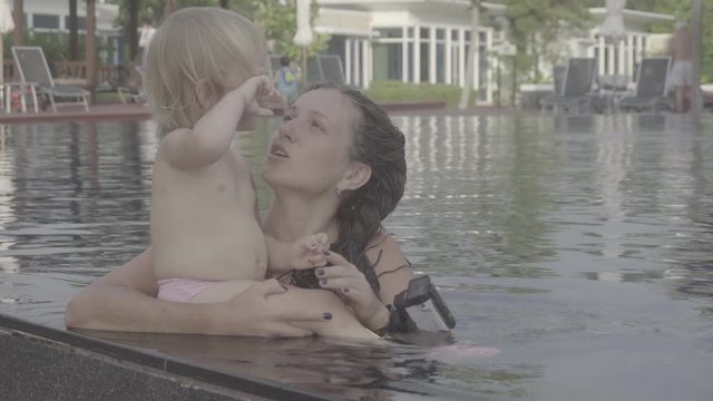 PHUKET, THAILAND - NOVEMBER 27, 2016: Mom with long braids talking with her little daughter in the pool. S-log, ungraded