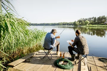 Photo sur Plexiglas Pêcher Landscape view on the beautiful lake and green reeds with two men fishing on the wooden pier during the morning light