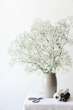 Bobbins of string and scissors on a white table top with a bouquet of white baby's breath preparing to make a floral wreath.