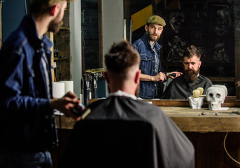 Barber preparing hair clipper for bearded man, barbershop background. Hipster lifestyle concept....