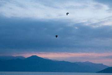 Sunrise on the lake. Panorama of the early morning. mountain in silhouettes and the rays of the rising sun. Birds flying in the sky. Sunrise on Lake Garda, Italy