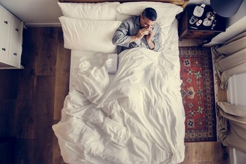 Sick man on the bed blowing his nose - obrazy, fototapety, plakaty
