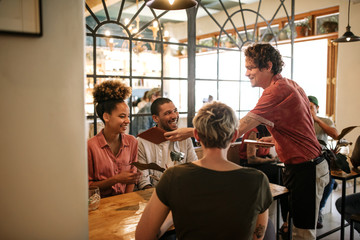 Group of smiling friends ordering food from a bistro waiter 