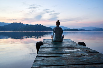 Woman sitting on dock at sunset on Lake Bunyonyi, Uganda, East Africa