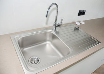 Close up on modern kitchen metal faucet and metal kitchen sink.