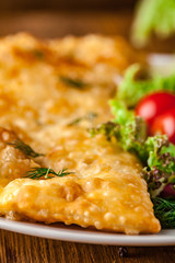Uzbek eastern Tatar cuisine, cheburek with meat and suluguni cheese in a white plate with vegetables and greens on a wooden table.