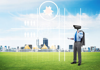 Camera headed man standing on green grass against modern cityscape