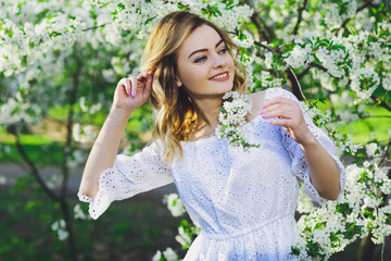 Beautiful blonde girl with blond hair in a dress on a background of spring blooming trees