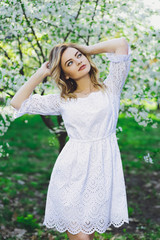 Fototapeta na wymiar Beautiful blonde girl with blond hair in a dress on a background of spring blooming trees