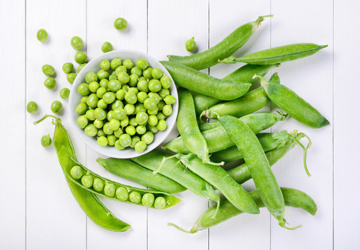 Fresh peas on white wood background. Top view