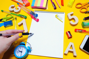 the student makes notes in a notebook. copy space. school accessories on a desk on a yellow background. concept of education. stationery. watches, colored pens, phone, markers. 