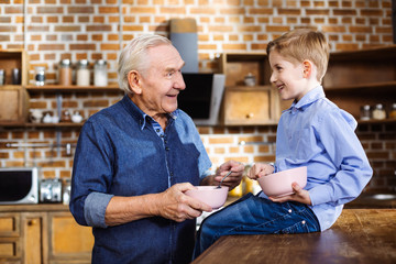 Positive aged man enjoying breakfast with his grandson