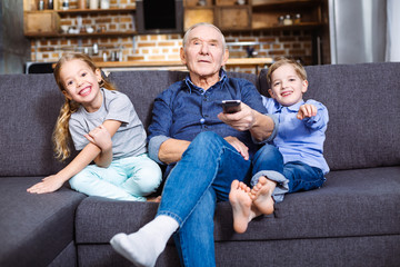 Caring retired man watching TV with his grandchildren