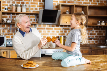Joyful aged man and his granddaughter eating home made pastry