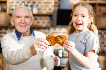Cheerful elderly man eating cookies with his granddaughter