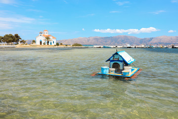 House for ducks on the water in the Elafonisos village on the background of Agios Spyridon church and picturesque seascape. Elafonisos island, Laconia, Peloponnese, Greece June 2018.