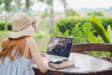 Fototapeta premium Young cute brown hair woman wearing cream hat using laptop notebook for education and writing text in a natural park, Technology social media concept.