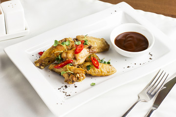 Grilled baked chicken wings with chili pepper and hot sauce on white plate