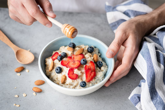 Eating healthy breakfast oatmeal porridge with fresh berries, honey and nuts. Selective focus