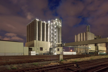 Illuminated petrochemical production plant against a cloudy blue sky at night, Antwerp, Belgium.