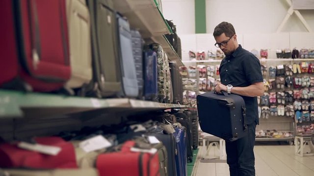 Man trying to fing new suitcase for a trip. Man preparing for vacation. Shopping for a new bag. Nice, big luggage. Checks on the handle.