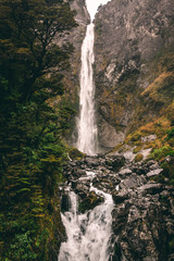 Water fall from mountains running into stream with dark rocks