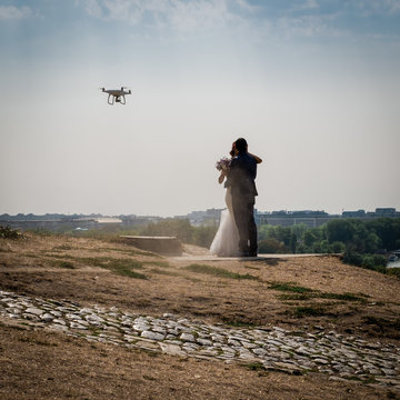 Two newlyweds kissing while a drone takes them. Belgrade on the background