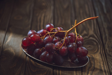 close-up shot of branch of ripe grapes on vintage metal plate on rustic wooden table