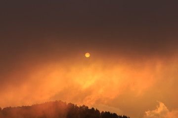 Reddish sun covered by clouds at sunset.Concept atmospheric phenomena