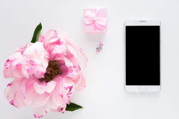 White background with copy space, smart phone lying on the table, pink peony flower, earrings, small gift for girl, advertising space, top view