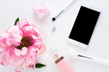 Obraz na płótnie Canvas White background with copy space, smart phone lying on the table, pink peony flower, makeup brushes, perfume bottle, earrings, small gift for girl, advertising space, top view