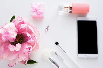 White background with copy space, smart phone lying on the table, pink peony flower, makeup brushes, perfume bottle, earrings, small gift for girl, advertising space, top view