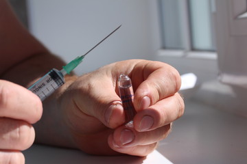 A doctor opened ampoule and hold it in one hand and a syringe in another.
