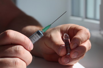 A doctor opened ampoule and hold it in one hand and a syringe in another.
