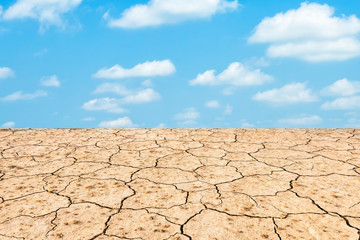 Brown dry soil or cracked ground texture on blue sky background texture with white clouds.