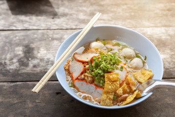 Close-up of Thai Noodle Soup with Meat in white bowl on wooden background.