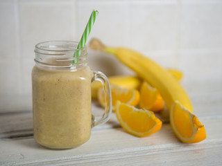 Fresh banana and orange smoothie on wooden white table